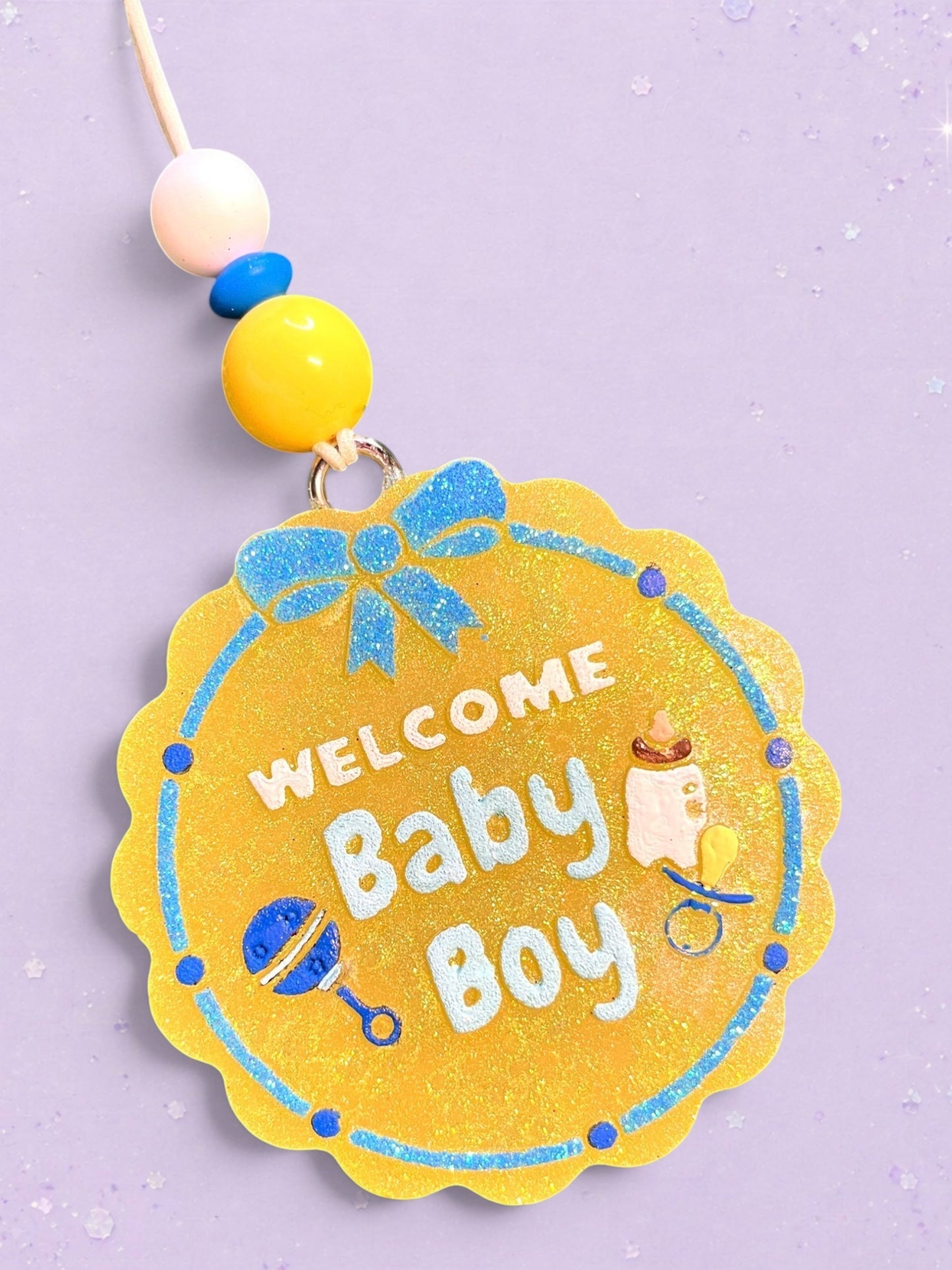 BeFreshie Welcome Baby Boy car freshie with yellow glitter, blue bow, rattle, and baby bottle on a purple background.