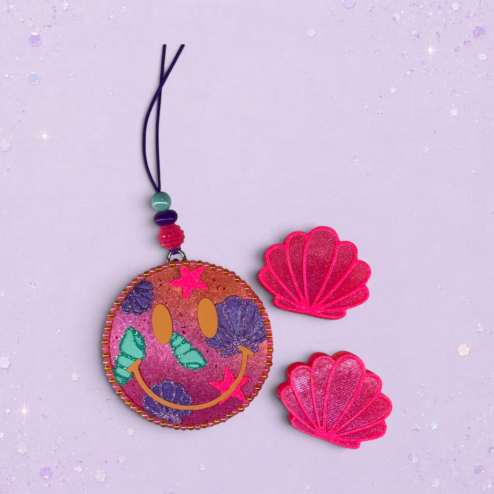 BeFreshie Happy Face Shells freshie with pink and purple glitter, featuring a smiley face, stars, and shell designs. Includes two pink shell accents.