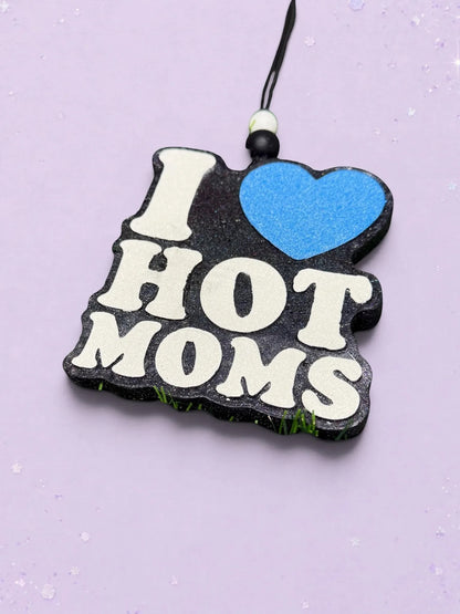 BeFreshie I Love Hot Moms car freshie with black glitter base, white text, and a blue heart on a light purple background.