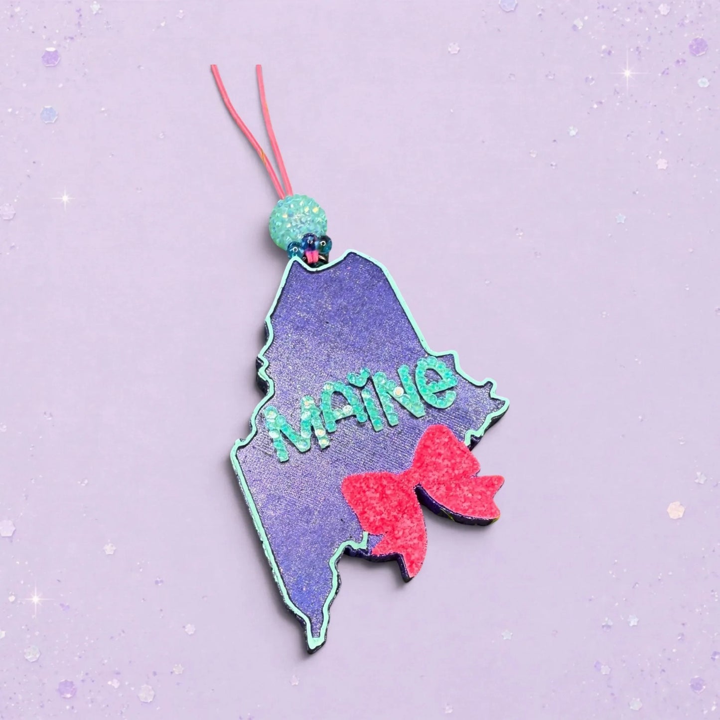 BeFreshie Maine state shape freshie with glittery teal lettering and a pink glitter bow.
