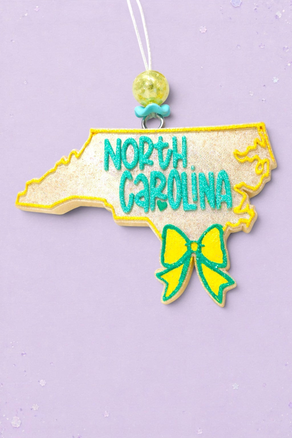 BeFreshie North Carolina state shaped car freshie with glittery gold finish, teal lettering, and a yellow bow.