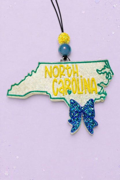 BeFreshie North Carolina state shaped car freshie with glittery white finish, yellow lettering, and a blue glitter bow.