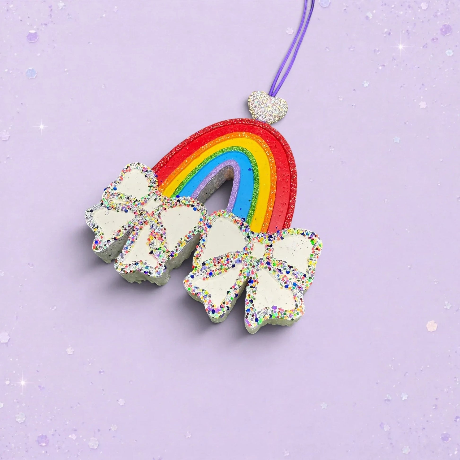 BeFreshie rainbow car freshie with white glitter bows and a heart charm in Ghost Story scent on a purple background.