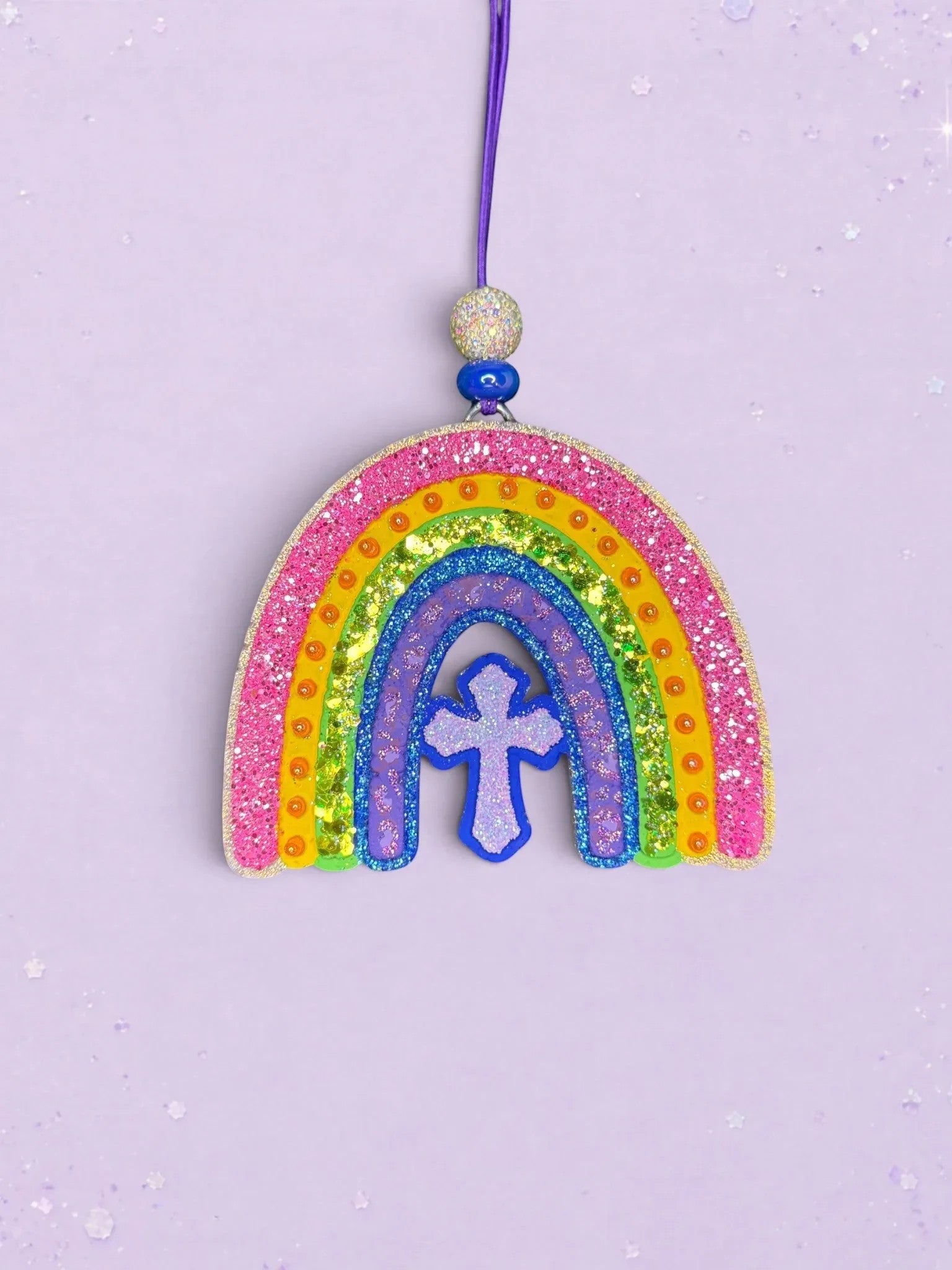 BeFreshie rainbow and cross car freshie with vibrant glittery stripes and a purple hanging cord on a lilac background