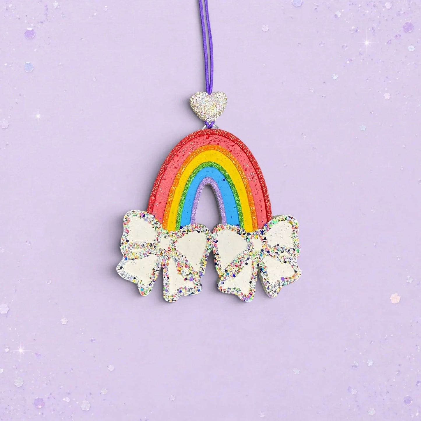 BeFreshie rainbow car freshie with white glitter bows and a heart charm, scented Ghost Story on a purple string.