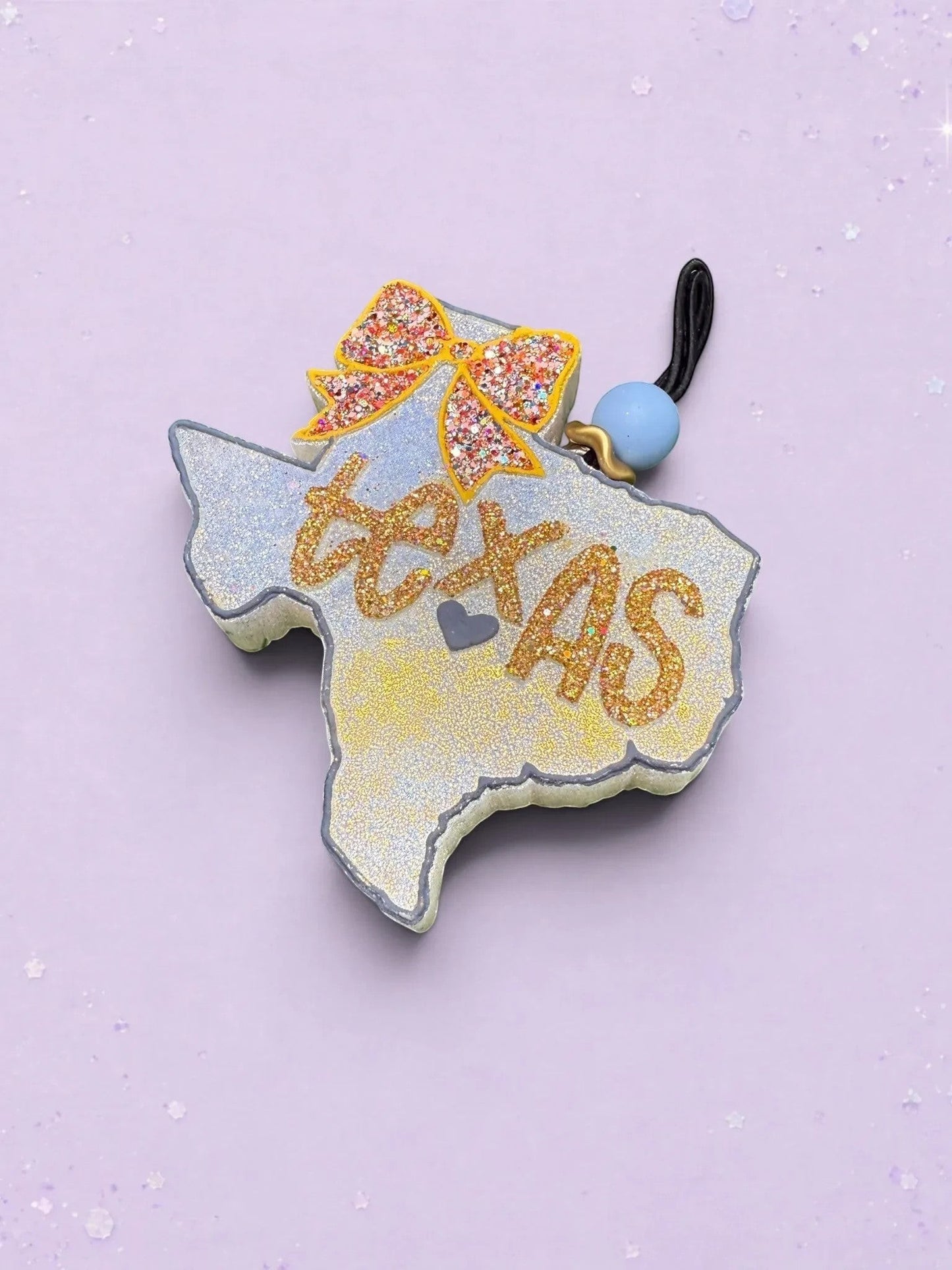 BeFreshie Texas shaped car air freshener with a glittery orange bow and gold glitter text on a light purple background.