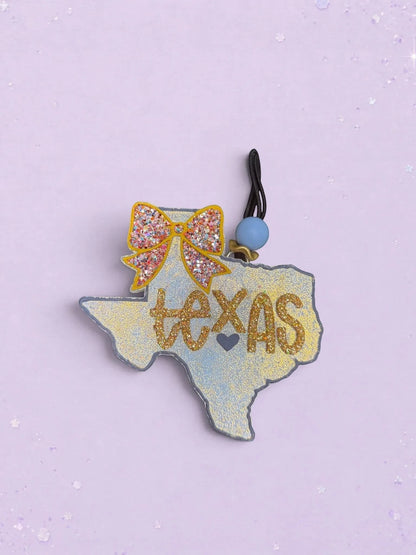 BeFreshie Texas shaped car air freshener with a glittery gold bow and script text on a light blue background.